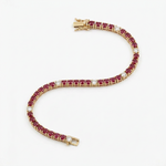 A yellow gold tennis bracelet featuring rows of round-cut deep red rubies and smaller clear diamonds, arranged in a curved S-shape on a clean white background.