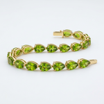 A yellow gold tennis bracelet featuring a row of marquise-cut green peridot gemstones, displayed on a clean white background.