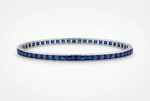 A tennis bracelet featuring square-cut deep blue sapphires set in a polished silver-colored metal, shown against a clean white background.