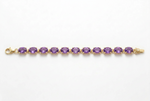 A yellow gold tennis bracelet featuring a row of round-cut purple amethyst gemstones, displayed horizontally on a clean white background.